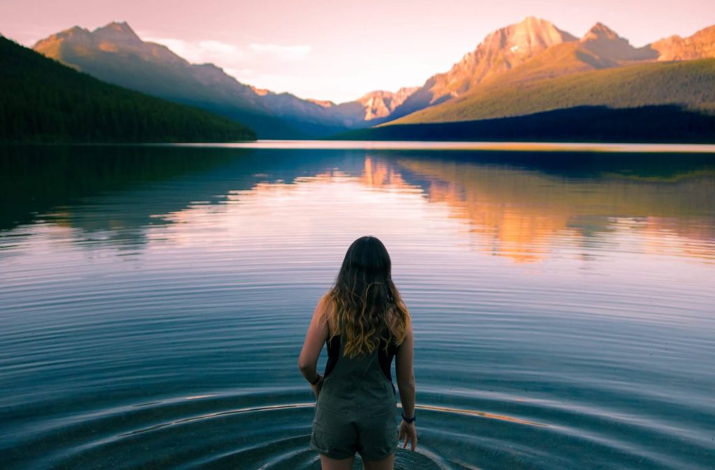 Una mujer vadeando el lago al atardecer, con montañas en primer plano