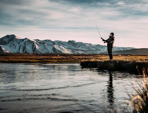 Una persona pescando en un lago con montañas nevadas de fondo